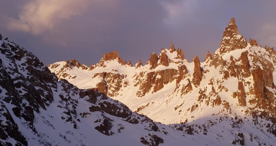 Snow covered mountains sit under the cloudy sky at sunrise