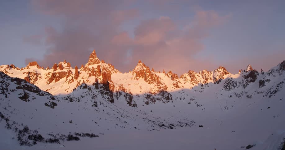 Snow covered mountains sit under a cloudy blue sky at sunrise