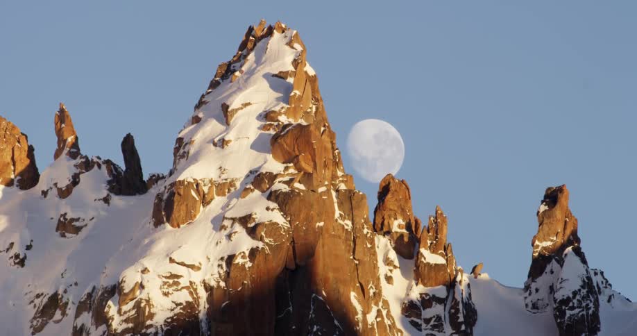 Snow partially covers the mountains as the moon is behind them