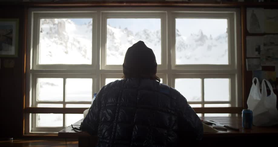 Silhouette of a person sitting in a table inside a mountain hut