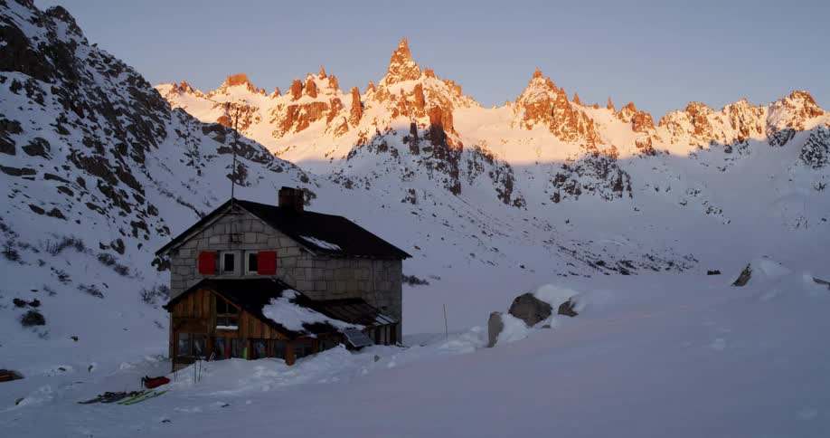 Two story house sits in shadow of mountain as sun highlights ridge in background