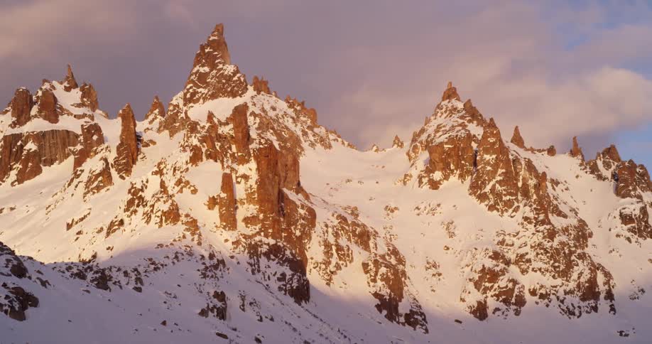 Snow covered mountains sit under a cloudy blue sky