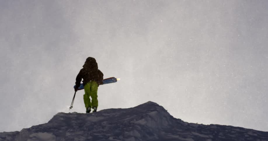 A lone skier hikes up a mountain while snow blows all around