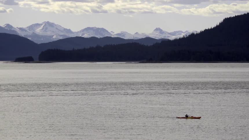 A person rows their boat near mountains on a cloudy day