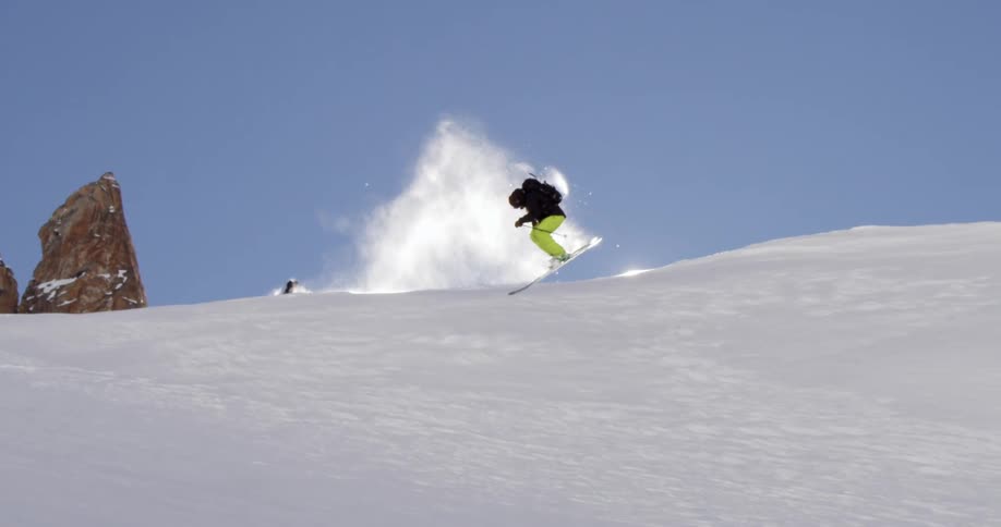 A skier jumps and spins as a dog runs behind him