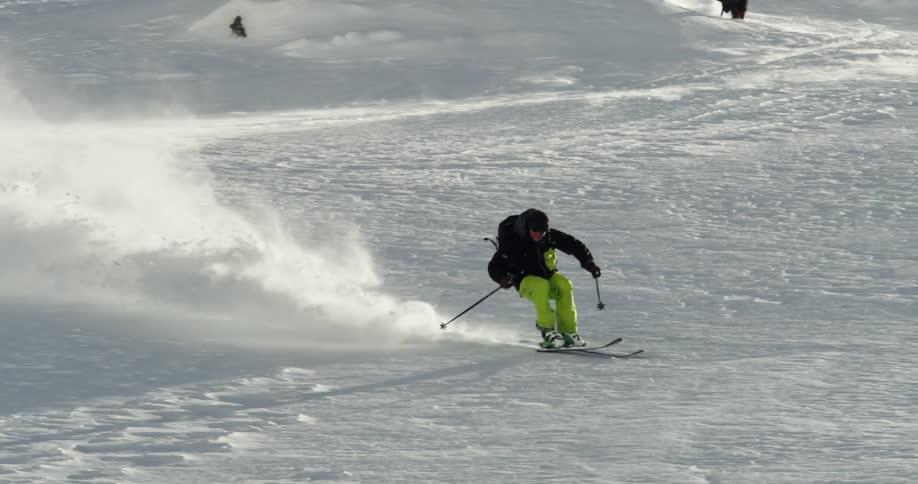 A person skiing down a snowy mountain with a dog running behind him