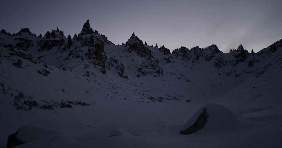 The sky darkens over a jagged mountain range in winter