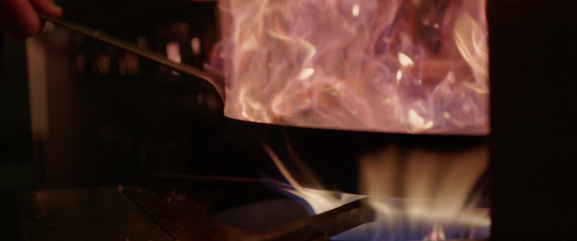 A person is cooking with a pan full of flames on a stove