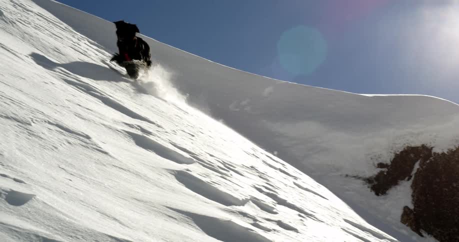 Dog runs on the side of a snow covered hill on a sunny day