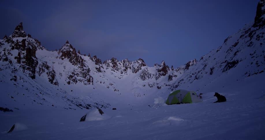 A dog outside a tent camping in snowy mountains