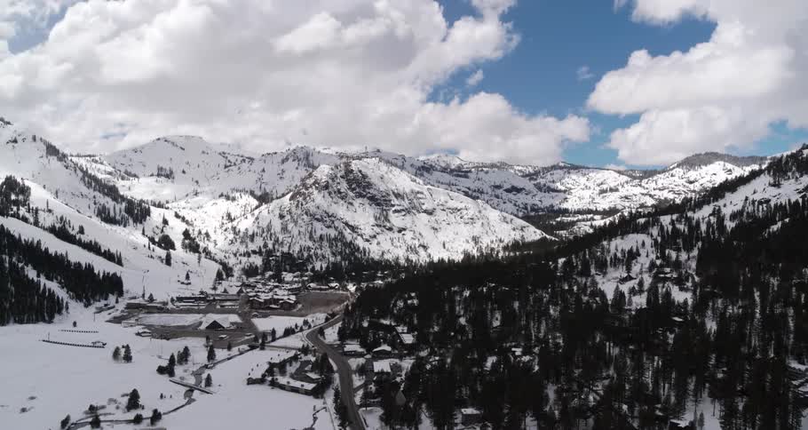 A snow covered mountain range and forest with a parking lot at the bottom