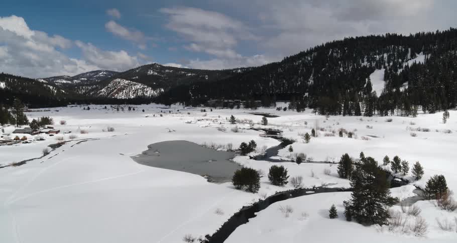 A river surrounded by snow and trees with a mountain range and the sky in the background