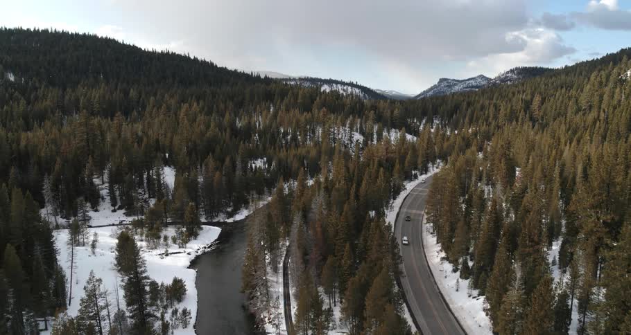 Aerial view of a highway between a snowy mountain and a narrow river