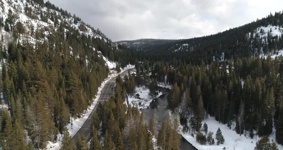 Sparse traffic along a road through an evergreen forest in the valley of a snow mountain range
