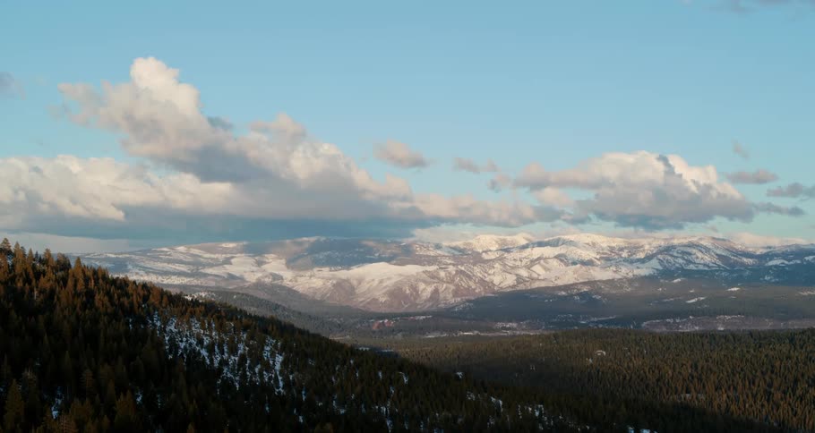 Conifer forest occupies snow covered mountain slope on opposite side of valley from mountains