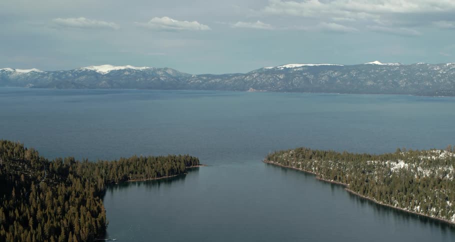 Aerial view of a great lake surrounded by snow covered pine forests near the mountains