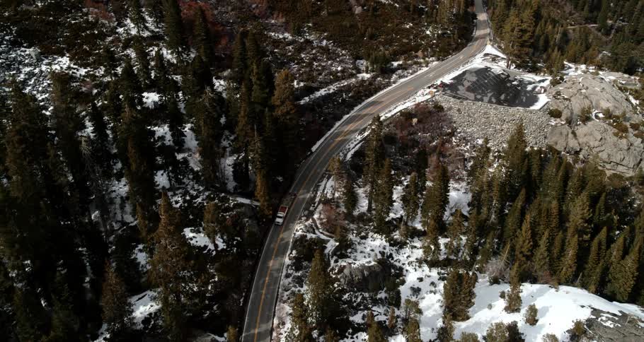 A truck towing a trailer makes its way up a road that passes through a forested mountain range