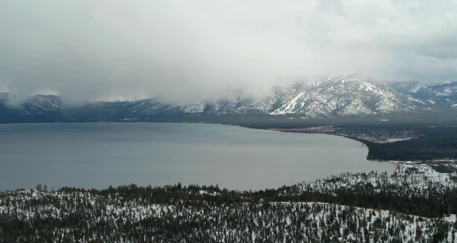 Low lying clouds obscure snowy mountain bordering circular coast covered in snowy forest