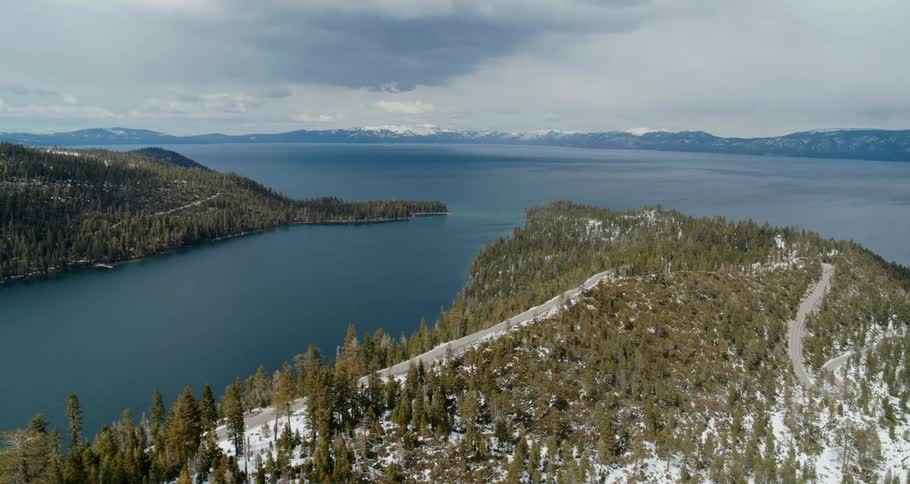 An aerial view with a forest a body of water and mountains in the far distance
