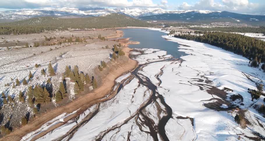 Aerial view of a frozen river surrounded by pine trees near the mountains