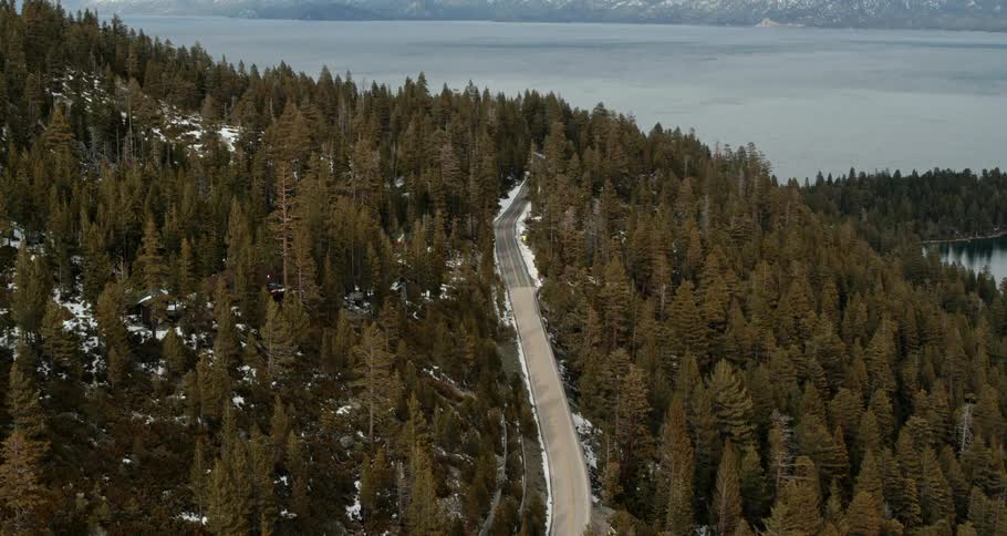 A road runs through a woodland on a hill next to a large lake