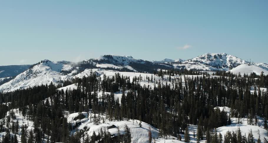 A mountain range covered in snow with trees with the sky and clouds in the background