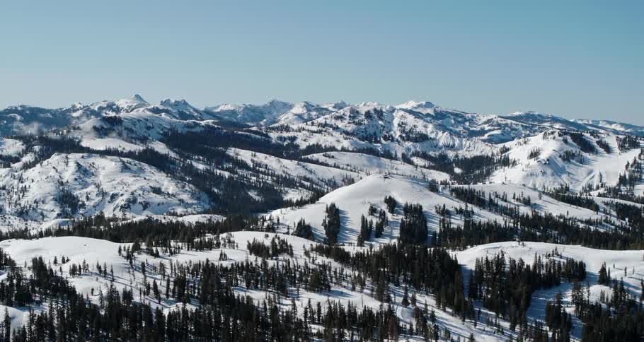 A snow covered mountain range with trees with the sky and clouds in the background