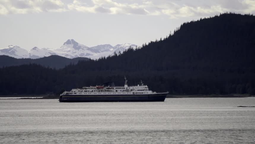 A large boat moves beside the hilly shore