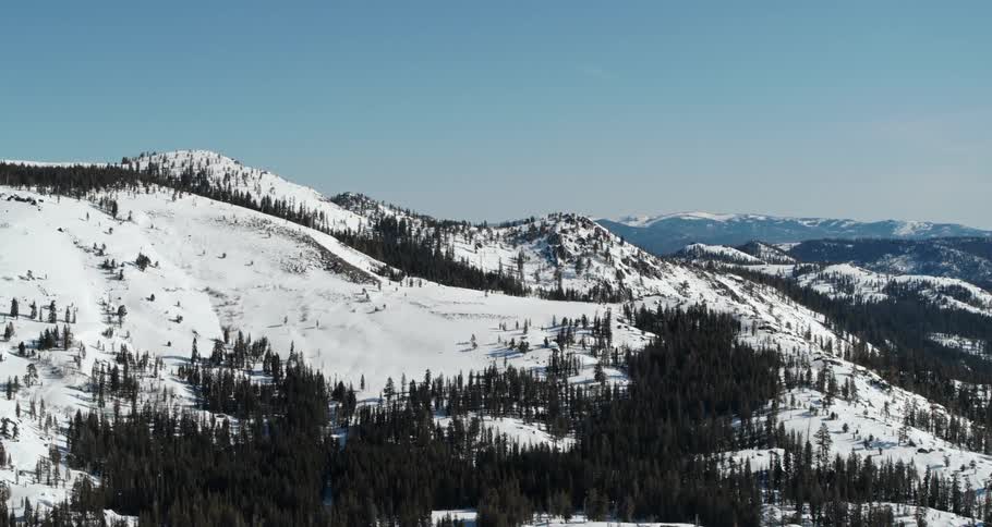 An aerial view of snowy mountains covered in pine trees in the wilderness