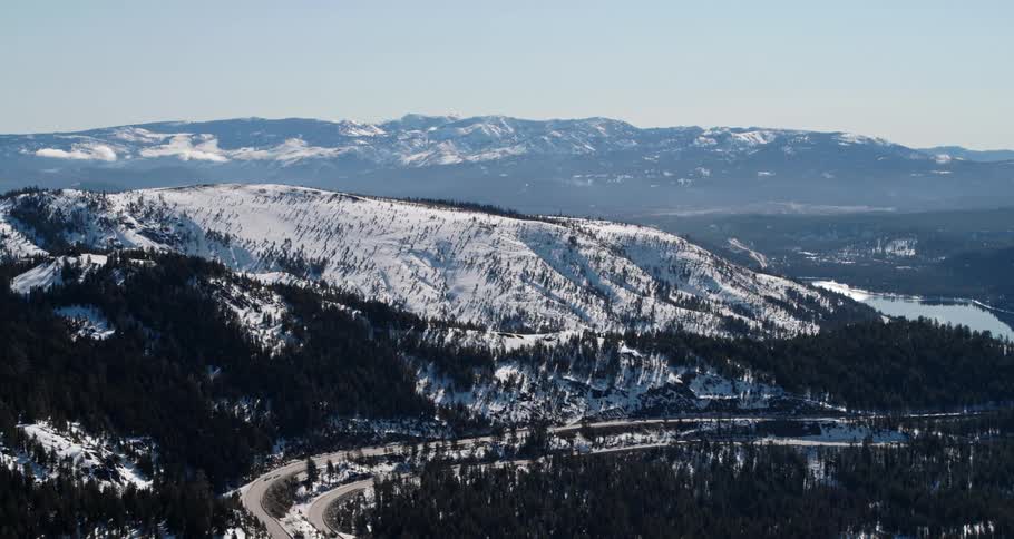 Aerial view of a vehicle driving on a road by a snow covered forest