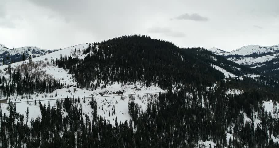 A hill covered with snow with trees with the sky and clouds in the background