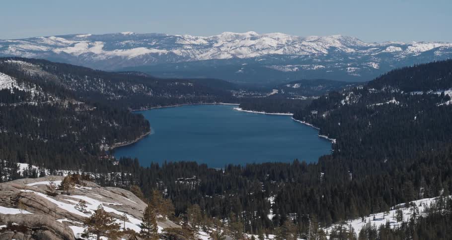 A lake surrounded by trees with a mountain range the sky and clouds in the background