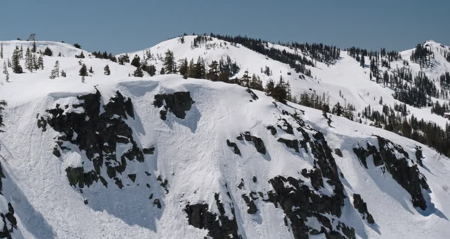 A mountain ridge covered in evergreen trees and snow under a clear sky