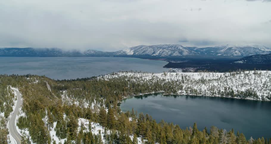 Two lakes divided by land and trees with a mountain range and the sky in the background