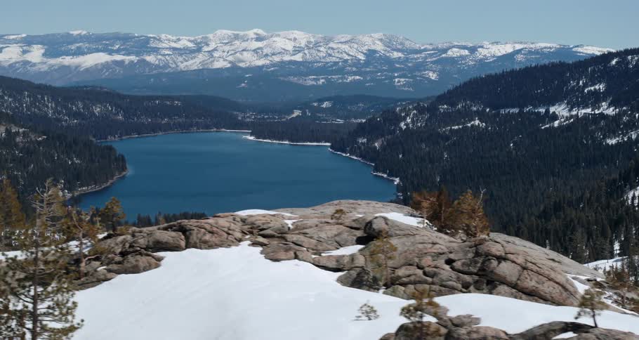 A small lake is surrounded by a forest and snow capped mountains