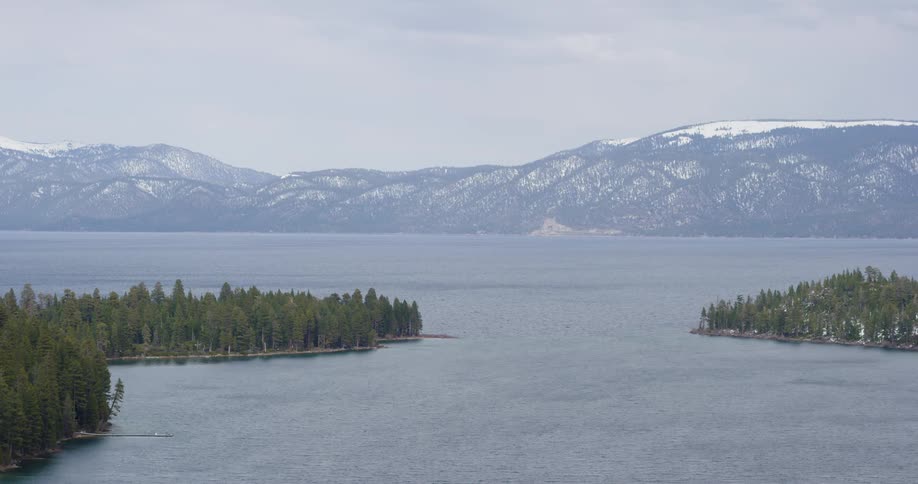 Aerial view of a great lake surrounded by pine trees near the snow covered mountains