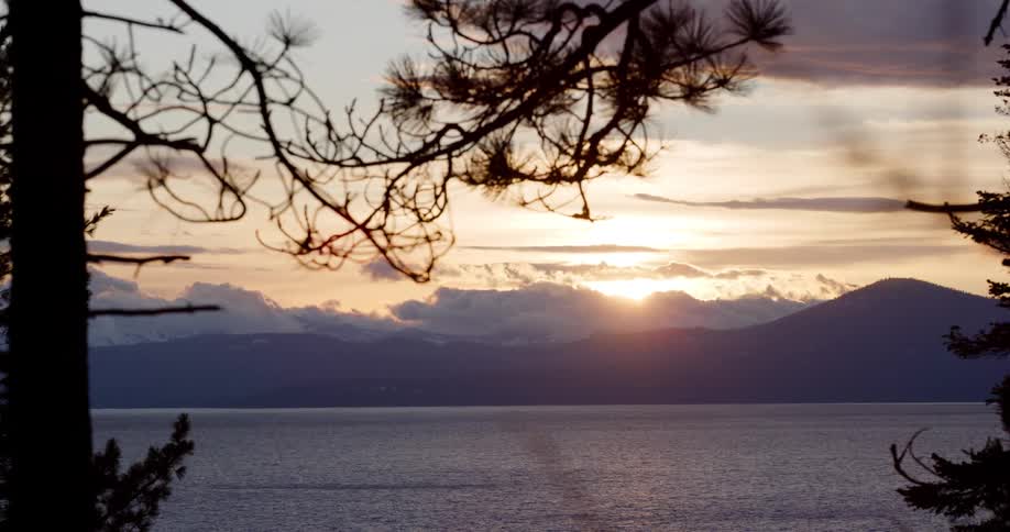 The sun sets over a mountain lake with silhouetted pine trees