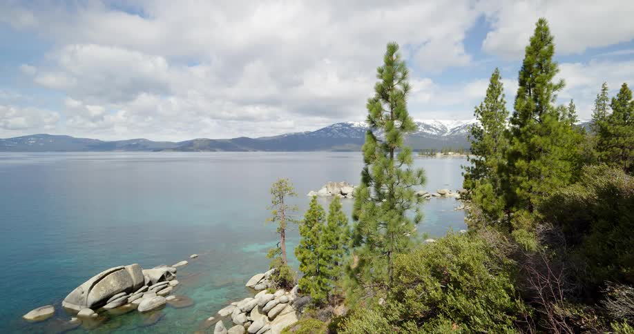 The rocky shoreline of a lake surrounded by mountains and woodland