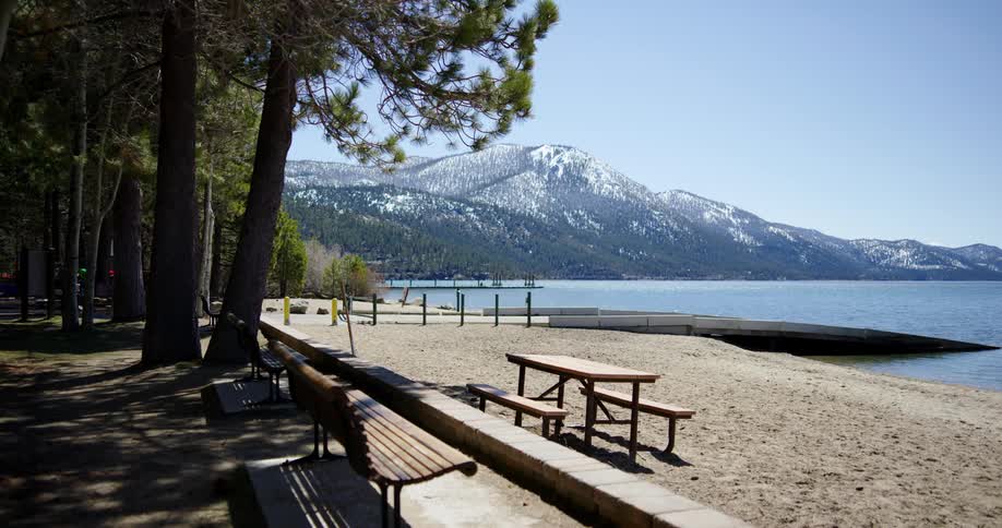 A park on the coast of a lake bordering a snowy mountain