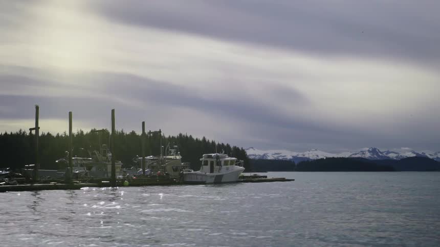 Boats sit at dock on a lake with forest and snow covered mountains in the background