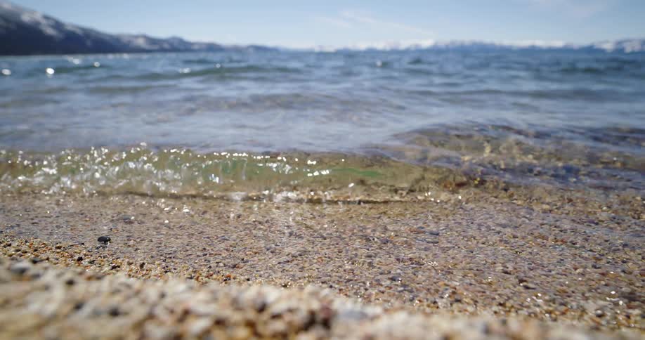 Small waves of crystal clear water washes up onto a gravel covered shoreline