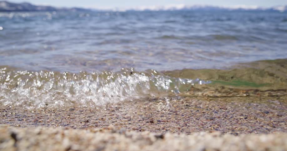 Small ocean waves break against coast with distant snowy mountains in the background