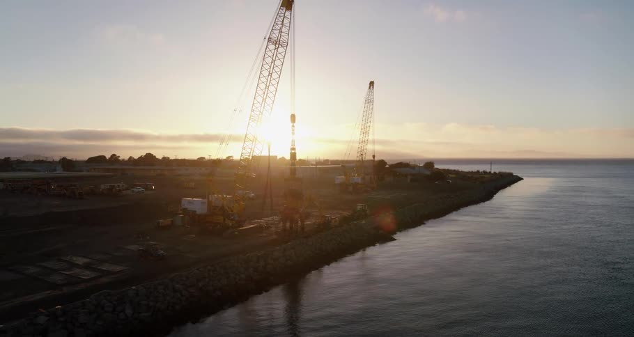 Construction cranes near a coast with water with the sky and clouds in the background