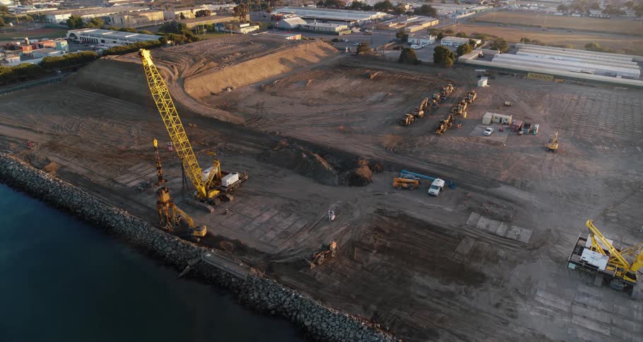 A construction site with many cranes on a river bank