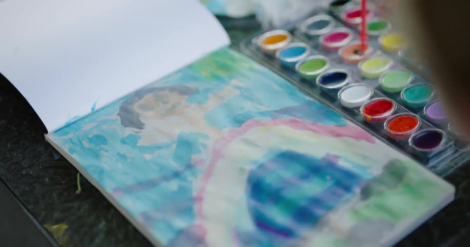 A youngster is making a painting for fun while using a tray full of watercolor paints and a small brush