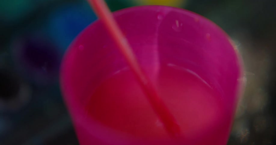A person rinses off a paintbrush in a pink cup