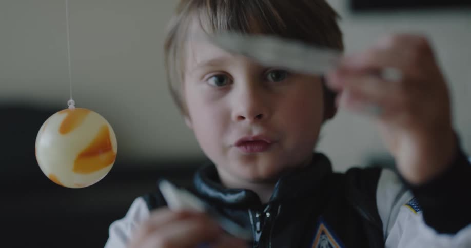 A little boy plays with a toy rocket ship where a pretend planet hangs