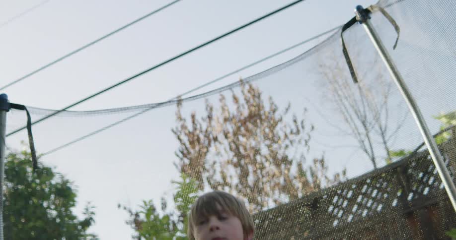 A little boy in a space suit jumping on a trampoline in a back yard