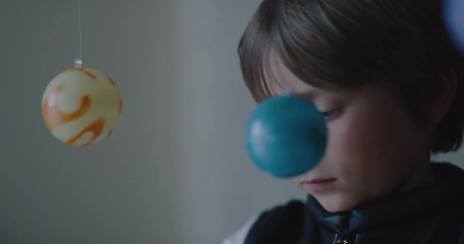 A little boy playing inside with a toy spaceship and toy planets