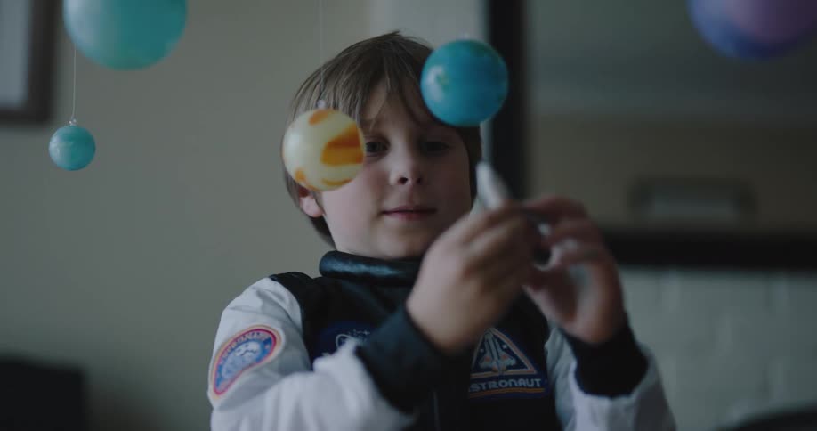 A little boy in a space suit plays with a toy rocket ship and planets at home